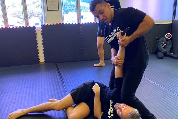 An instructor controlling a knife-wielding arm during a bodyguard training session on the studio mats