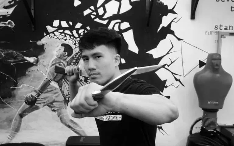 Black-and-white photo of a Kali (Filipino Martial Arts) practitioner holding two training blades in guard at the JEET Academy KL studio