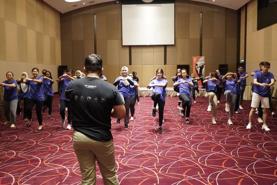 A corporate team in matching t-shirts drilling self-defence stances in a hotel ballroom